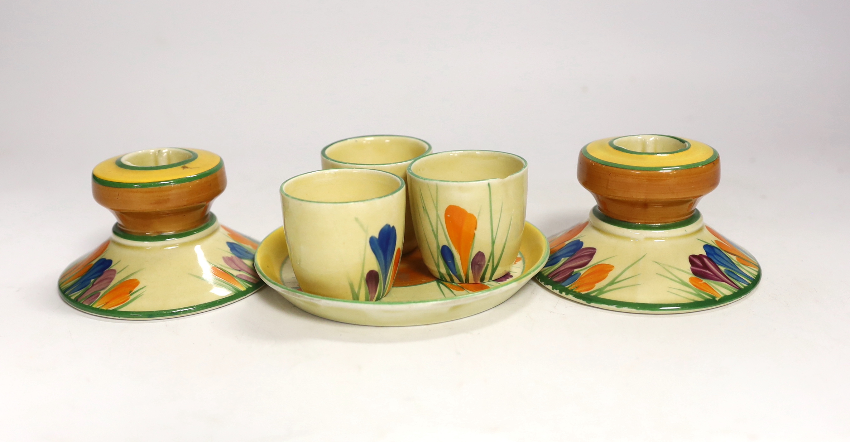 Clarice Cliff Crocus pattern items; a pair of candlesticks, 5cm high and three egg cups with stand